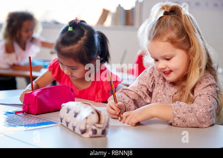 Two young schoolgirls sitting at a desk in an infant school classroom working, close up Stock Photo
