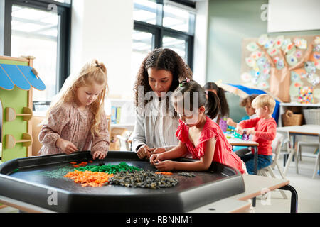 Two young schoolgirls standing at a table playing a game with their female teacher in an infant school classroom, selective focus