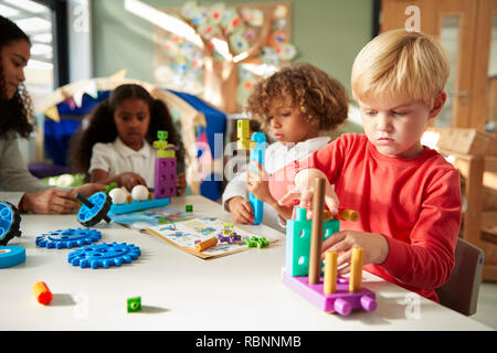 Infant school boy sitting at a table using educational construction toys with his classmates, close up Stock Photo