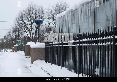From the roof hanging long icicles in the foreground metal fence and a sign in the distance with the inscription in Russian '2nd Garden bridge' (St.Pe Stock Photo