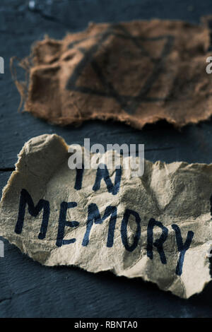 closeup of a ragged jewish badge and a yellowish piece of paper with the text in memory written in it, on a gray rustic wooden surface Stock Photo