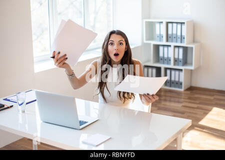 Surprised businesswoman reading paper at workplace in office. Business woman frustrated and stressed with new contract Stock Photo