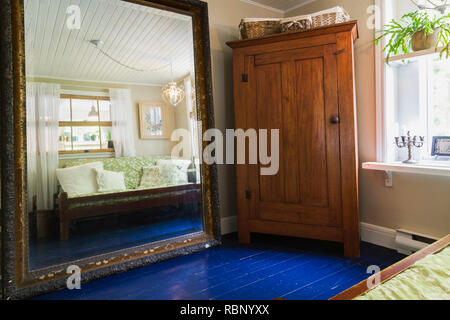 Guest bedroom with wood-frame single bed, large mirror and old wooden armoire inside an old 1862 cottage style home Stock Photo