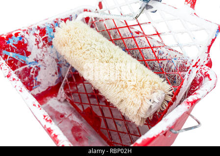 Used, red, dirty, paint bucket with paint roller lies on the grid. Isolated on a white background with a clipping path. Stock Photo