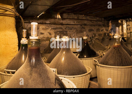 Homemade red wine stored in large glass jugs in baskets in the basement inside an old circa 1850 Canadiana cottage style home Stock Photo