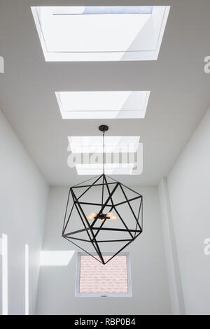 Skylight windows and black steel hexagonal lighting fixture with five clear glass bulbs hung above the staircase inside a modern cube style home, Queb Stock Photo