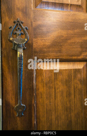 Close-up of antique brass metal handle with decorative details on a wooden closet door inside Renaissance period style home. Stock Photo