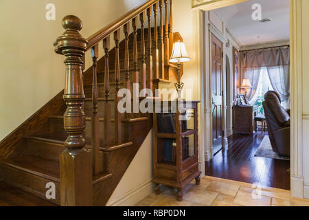 Brown stained oak wood staircase and living room through doorway inside Renaissance period style home. Stock Photo