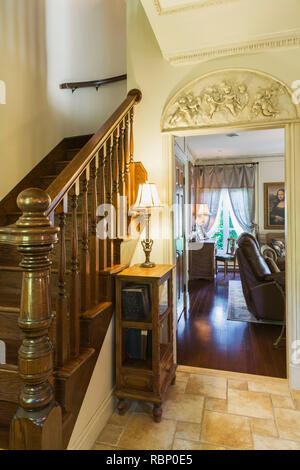 Brown stained oak wood staircase and living room through doorway inside Renaissance period style home. Stock Photo