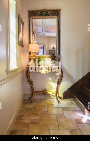 Antique wooden console with statue and illuminated lamp in main entryway inside a Renaissance period style home. Stock Photo