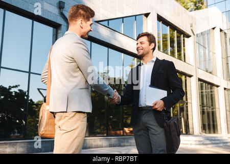 Two confident businessmen standing outdoors, shaking hands Stock Photo
