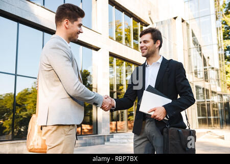 Two confident businessmen standing outdoors, shaking hands Stock Photo