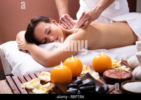 Male Therapist's Hand Giving Shoulder Massage To Relaxed Young Woman Stock Photo