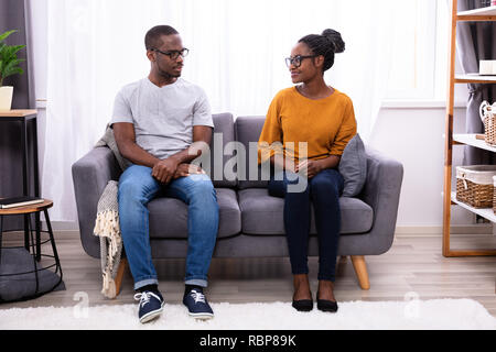 An African Young Couple Sitting On Sofa Looking At Each Other Stock Photo