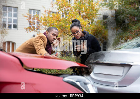 Man And Woman Looking At Smoke Coming Out From Car's Engine After Accident Stock Photo