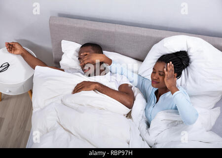 Disturbed Young African Woman Holding Her Husband's Nose To Stop Him From Snoring On Bed Stock Photo