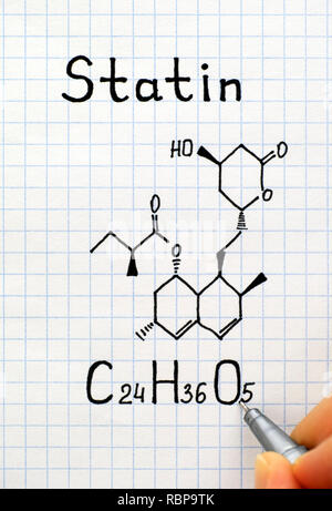 Person fingers with pen writing chemical formula of Statin. Close-up. Stock Photo