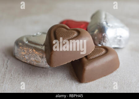 Group of chocolates on tan tile.  Two unwrapped, two in silver wrap, and one red.  close up shot.  landscapped. Stock Photo