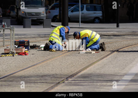 Two workers sitting on their knees are repairing gutter at tramway rails in the city Stock Photo