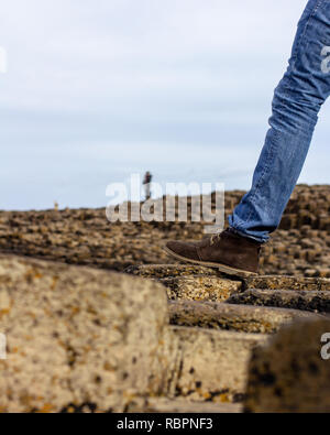 Blue jean clad leg and brown boot wearing foot of hiker on rocks, unidentifiable people in the distance Stock Photo