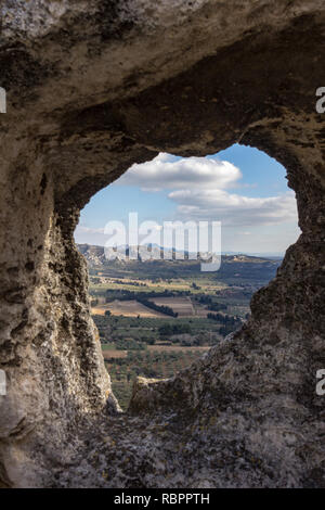 The valley between Les Baux de Provence and the Alpilles mountains are dotted with farms as viewed through a natural frame in the wall Stock Photo