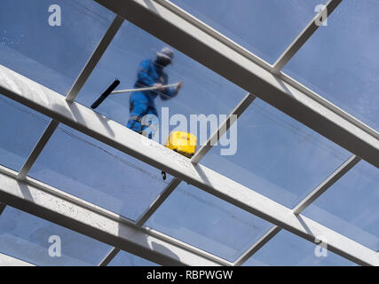 Worker cleaning large glass roof over swimming pool Stock Photo