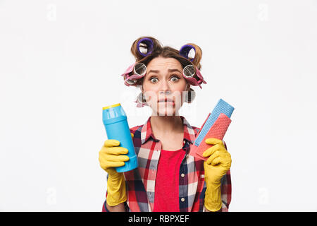 Upset housewife with curlers in hair standing isolated over white background, holding detergents Stock Photo