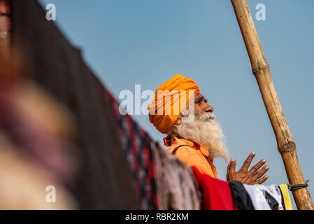 A holy man in prayer with his hands folded framed by a pole and clothes line in Varanasi, India Stock Photo