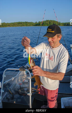 Finnish fisherman on a boat caught a pike spinning and removes it from the lure Stock Photo