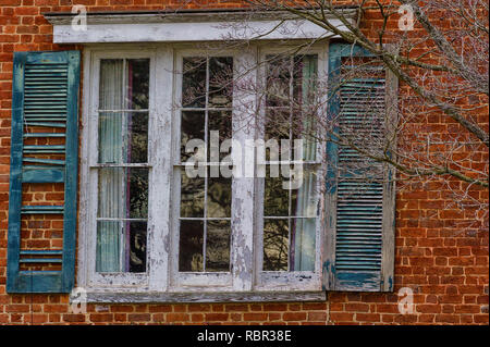 Decaying shutters on a paint peeling window that is part of a brick structure. Stock Photo