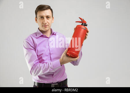 young man holding a fire extinguisher in his hands isolated on a light background Stock Photo