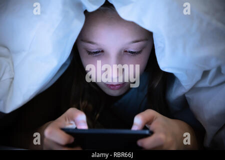 Girl Under White Blanket Using Digital Tablet Stock Photo