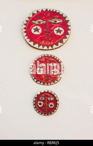 Dishes. Three red plates with the image of the sun on a white wall background. Mijas, Andalusia, Spain. Stock Photo