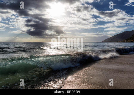 Sun shining through the clouds at sandy beach with waves Stock Photo