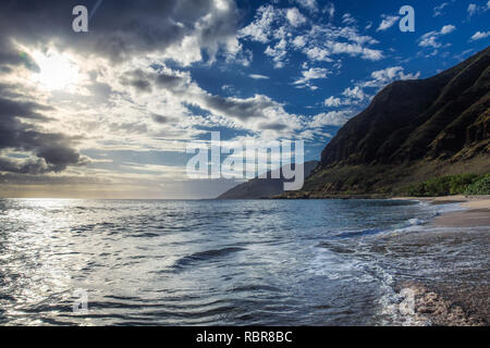 Sun shining through the clouds at sandy beach with waves Stock Photo