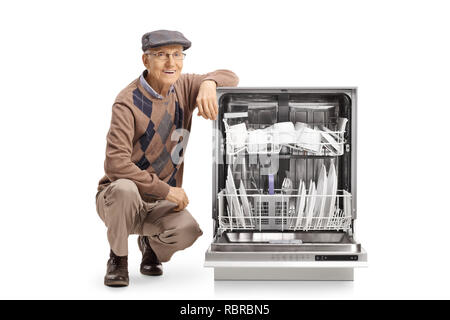 Senior man kneeling next to a loaded dishwasher isolated on white background Stock Photo
