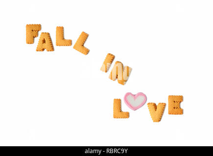 The word FALL IN LOVE spelled with alphabet shaped biscuits and a heart shaped marshmallow candy on white background, Valentine's day Stock Photo