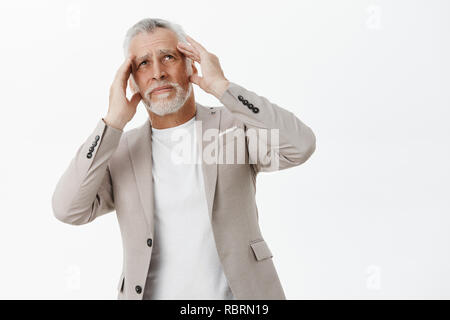 Portrait of old man having headache from bothering loud noise from neighbours living upstairs holding hands on head bending body and looking up with bothered and irritated expression Stock Photo