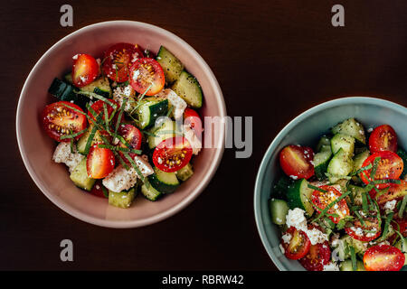 Ceramic bowls of Mediterranean Greek salad with cherry tomatoes, cucumber, feta cheese, extra virgin olive oil and black pepper Stock Photo