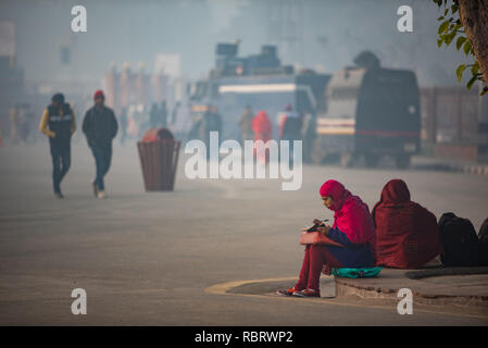 Early morning scene in front of the Red Fort in Delhi with woman sitting and writing on her notebook and pedestrians in the background. Stock Photo