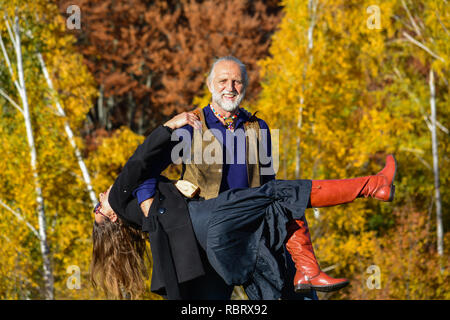 Happy, vital elderly couple dancing and having fun in a bright, sunny day on mountain meadow and birch forest in background Stock Photo