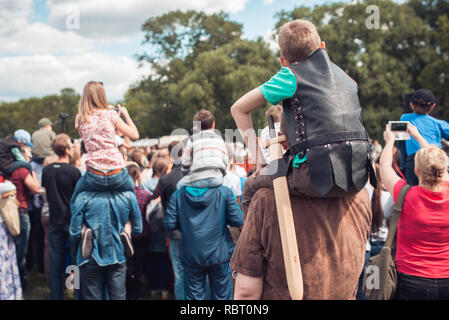 happy family on a festival. fathers, mothers and theirs children daughters having fun and playing in nature. the child sits on the shoulders of his dad and look the one direction in front of people crowd Stock Photo