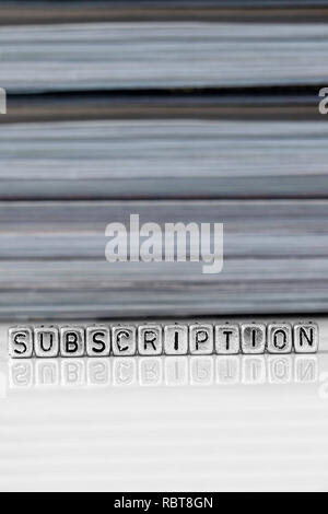 Subscription on beads with magazines stacked in the background reflected on a white surface Stock Photo