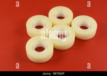Rolls of invisible matte adhesive tape on red wooden background Stock Photo