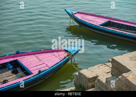 Composition with pink and blue boats docked on the Ghat in Varanasi in India: The river's water provides a green backdrop for the two colourful boats. Stock Photo