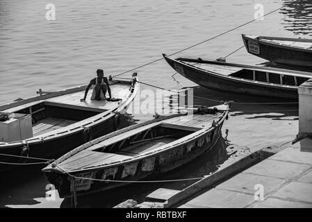Black and white photo composition of four boats on the Ganges with a man who forms the focus sits off-centre - in Varanasi, India. Stock Photo