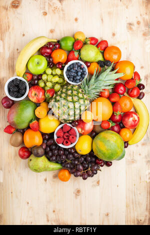 Circle filled with healthy colorful fruits, strawberries raspberries oranges plums apples kiwis grapes blueberries mango persimmon on light wooden Stock Photo