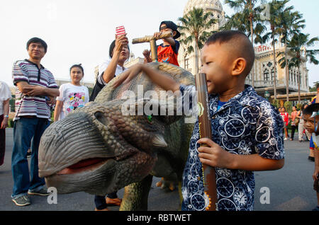 Children and parent stand next to a dinosaur statue during the Children's Day celebration at Government House in Bangkok. Stock Photo