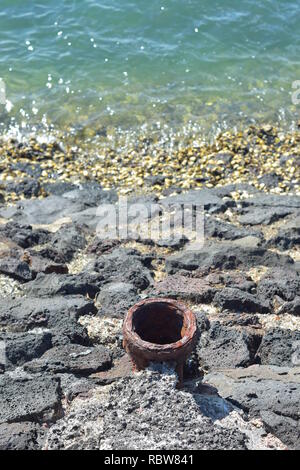 Rusty thick wall iron pipe protruding from sea wall made of cut stones and concrete. Note dense growth of oysters near and under sea surface. Stock Photo