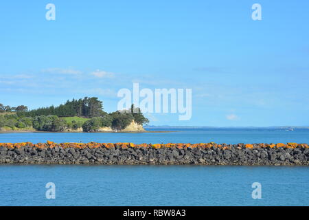 Sea wall made of free laid cut stone in blue sea on sunny day. Note bright yellow lichen growth on top of wall indicating areas where high tide water  Stock Photo